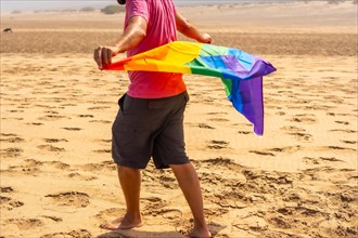 An unrecognizable gay person with the LGBT flag blowing in the wind in a desert