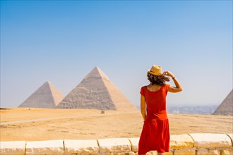 A young tourist in a red dress looking at the Pyramids of Giza