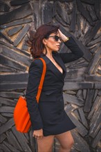 Fashion pose. Brunette girl in the city with sunglasses and red bag on a stone wall