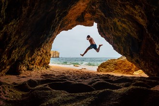 A man jumping into the natural cave in the Algarve on the beach at Praia da Coelha