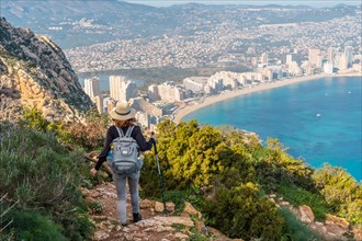 A young woman descending from the top of the Penon de Ifach Natural Park with the city of Calpe in the background
