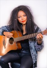 A closeup portrait of a stylish attractive female musician holding an acoustic guitar on her shoulder