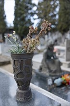Vase with withered flowers on a grave in a cemetery