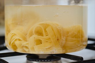 Closeup view of fettuccine pasta into boiling water in a transparent glass saucepan
