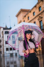 Posing of a young brunette Latina with a leather cap in the autumn rain with a transparent umbrella