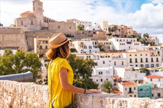 A young woman tourist looking at the cathedral of Santa Maria de la Neu from the castle wall of Ibiza