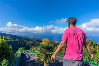 A young man in a pink t-shirt on top of the mountain at the viewpoint of the Cubo de la Galga natural park on the northeast coast on the island of La Palma