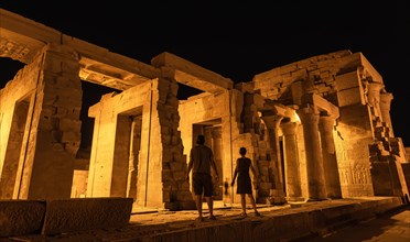 A couple of tourists between the columns at night of the temple of Kom Ombo in traditional dress
