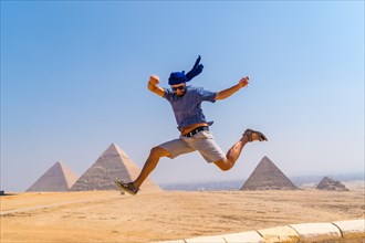 A young tourist jumping for joy in a blue turban and sunglasses at The Pyramids of Giza