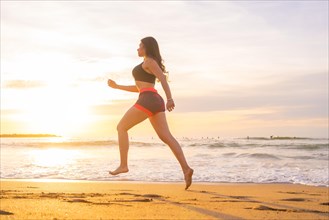 Horizontal photo with copy space of the side view of a young woman jogging along a beach during sunset