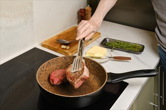 Close up view of flipping crispy beefsteak with kitchen tongs