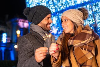 Winter portrait of a Caucasian couple enjoying the Christmas lights with torches in hand