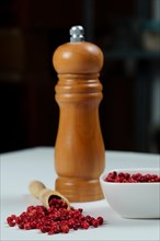 Pink peppercorns in a wooden spoon with a wooden pepper shaker isolated on a black background and copy space