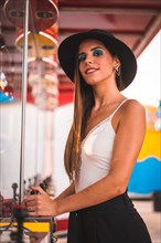 Smile of a young brunette with a black hat and white t-shirt enjoying in an amusement park on an arcade machine in summer
