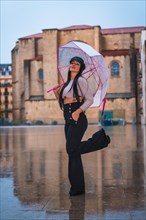 Posing of a young brunette Latina with a leather hat in the rain with a transparent umbrella in the city