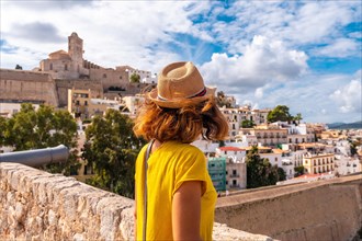 A young woman on vacation looking at the cathedral of Santa Maria de la Neu from the castle wall of Ibiza