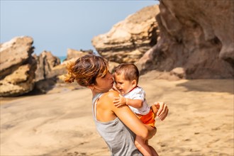 A young mother comforting her baby by the sea in Playa de Garcey