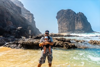 A young father with his baby in his backpack in the Roque del Moro of the Cofete beach of the natural park of Jandia