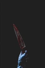 Upward pointing hand in blue glove holds bloodstained knife