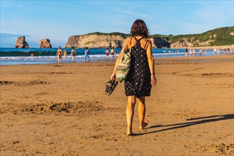 A young brunette in a black dress and sunglasses walking along the beach in Hendaye