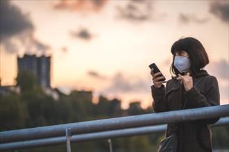 A young brunette with a mask on a sunset sending an audio message. First walks of the uncontrolled Covid-19 pandemic