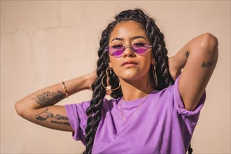 Urban session. Young dark-skinned woman with long braids wearing purple glasses on a plain background