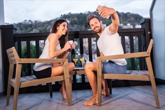 A Caucasian couple having breakfast on the hotel terrace in pajamas. Taking a selfie with the phone