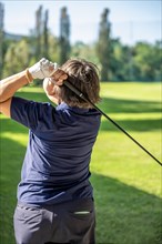 Rear View on a Female Golfer Making a Golf Swing in a Sunny Day in Switzerland