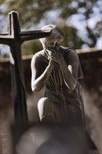 Mourning female figure in front of a cross in a cemetery