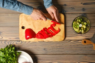 Top view of female hands slicing red bell pepper with kitchen knife