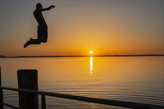 Boy jumps from the wooden jetty into the water at sunset