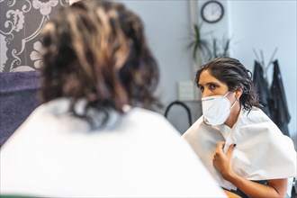 Client with face mask looking at how the tint looks on the mirror. Safety measures for hairdressers in the Covid-19 pandemic. New normal