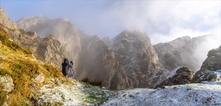Panoramic of a photographer taking a photo with the tripod in the snowy winter sunset
