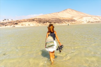 A young tourist walking through the crystal clear water on Sotavento beach one autumn morning in the south of Fuerteventura