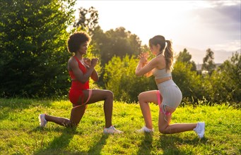 Caucasian blond girl and dark-skinned girl with afro hair doing stretching exercises in a park. Healthy life
