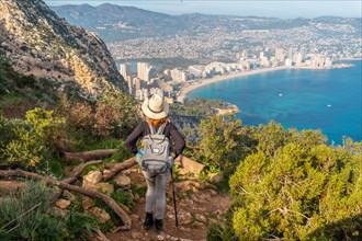 A young hiker on the descent path of the Penon de Ifach Natural Park with the city of Calpe in the background