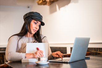 Latina brunette architect taking notes in online meeting from a coffee shop