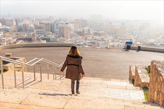 A young tourist at sunrise on the stairs of the viewpoint of Cerro San Cristobal and the city of Almeria in the background