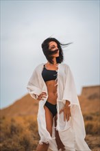 Brunette Caucasian model in a white dress and a black bikini in the Bardenas Reales desert