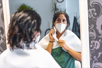 Client with face mask looking at herself with wet hair. Safety measures for hairdressers in the Covid-19 pandemic. New normal