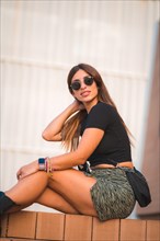 Street Style of an attractive young caucasian brunette sitting in the city with sunglasses