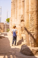 A young tourist in a white t-shirt and hat visiting the temple and looking at the ancient egyptian drawings on the columns of the Luxor Temple