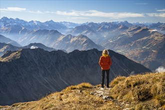 A hiker stands on the Nebelhorn and looks out over the Alps. Good weather with blue sky