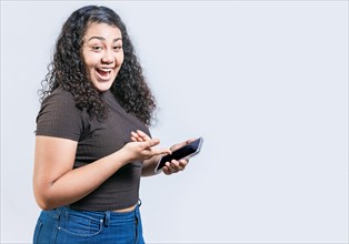 Smiling young woman holding cell phone and looking at camera. Happy latin girl using and pointing cell phone looking at camera isolated