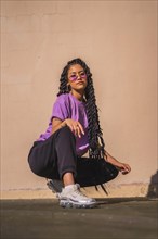 Urban session. Look of young dark-skinned woman with long braids putting on purple glasses