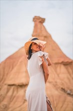 Sensual gazes of a brunette Caucasian girl in an explorer outfit with a white dress and a hat in a desert on a cloudy afternoon