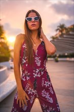 Sunset with a brunette in a maroon floral dress and white sunglasses enjoying the summer in the golden hour