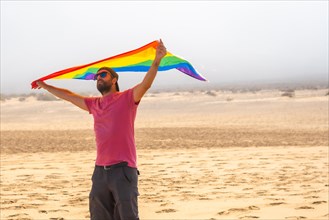 A gay person with the LGBT flag enjoying it moving with the wind in a desert