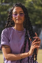 Young smiling dark-skinned woman in purple shirt holding long braids