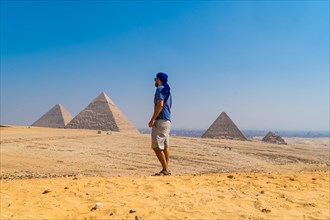 Portrait of a young man in a blue turban walking next to the Pyramids of Giza